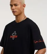 Remera negra de algodón con corte relaxed, cuello redondo y mangas cortas. Estampa frontal con una cruz y el nombre "Tupac Shakur" en color naranja.