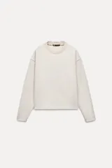 Sweater color crema de tejido suave, con cuello redondo en rib y mangas largas sin costuras.