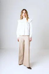 Blusa blanca de mangas largas con cuello alto con volados y detalles de encaje.