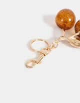 Llavero con dije de cerezas color marrón con glitter dorado, hojas doradas y mosquetón metálico dorado.