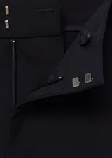 Pantalón negro de vestir, de tiro alto, corte recto y largo. Presenta cierre frontal con botón, gancho y cremallera oculta, trabillas, bolsillos laterales, pinzas delanteras, forro interior y bolsillo de ribete en la parte posterior.