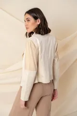 Chaqueta corta cruzada de cuero vegano color marfil, combinada con tela rayada color oro, con cierres metálicos y tachas doradas.