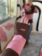 Buzo tejido de hilo color rosa y chocolate a rayas horizontales, con cuello redondo rojo y parche bordado en el pecho.