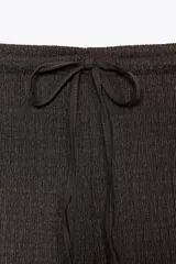 Pantalón de vestir color crudo, de tiro alto, corte recto y textura arrugada. Cuenta con cintura elástica ajustable con cordones.
