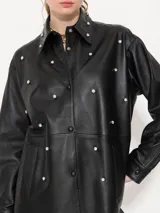 Camisa negra de cuero ovino con broches forrados en el mismo cuero, remaches con brillo en el delantero y cuello, y bolsillos con vista de cuero en el delantero.