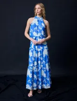 Vestido largo de gasa con estampado floral en tonos celeste y blanco. Tiene escote halter, cintura elastizada con lazo de ajuste, abertura en la espalda con botones y forro interno.