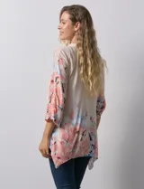 Blusa de gasa color beige con estampado floral en tonos rosa y celeste. Tiene cuello a la base, escote en V y abertura central con botones. Las mangas son 3/4 y regulables con presilla y botón.
