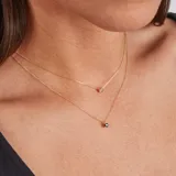 Conjunto de collar doble con cadena de oro amarillo 18k. El collar superior tiene un dije de zafiro engarzado en 4 puntas, y el collar inferior tiene un dije de flor negra con centro de zafiro.
