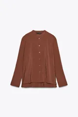 Camisa marrón de Zara Woman Collection confeccionada en hilatura con mezcla de lyocell. Tiene cuello redondo, manga larga acabada en puño, bajo asimétrico con aberturas laterales y cierre frontal con botones.