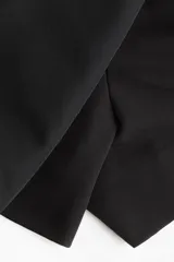 Short pollera negro de tiro alto con diseño cruzado tipo pareo en el frente, asegurado con un cinturón cosido y hebilla revestida. Presenta cierre oculto y cierre de corchete en un lateral.