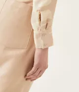 Camisa de crepé color beige con estampado geométrico en tonos neutros, cuello camisero, manga larga y cierre con botones. Tiene un lazo frontal para atar.