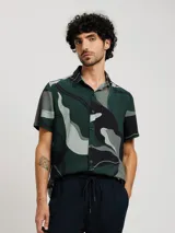 Camisa blanca de manga corta con estampado de hojas en negro y gris, cuello clásico y corte recto.