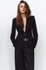 Blazer negra entallada con cuello solapa, manga larga con hombreras, bolsillos delanteros con solapa y cierre frontal con botones dorados.