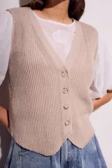 Chaleco de punto color beige con cuello en V y cierre frontal con botones.