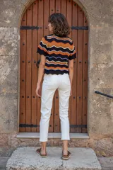 Chomba tejida de punto con cuello estilo polo y escote en V. De manga corta y calce relajado, cuenta con diseño de ondas horizontales en colores combinados: negro, naranja, blanco y lila.