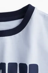 Remera celeste con cuello y mangas con ribete azul marino. Estampa frontal con la frase "Mi Amore" en azul marino.