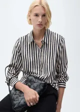 Camisa de manga larga con estampado de rayas verticales en blanco y negro, cuello camisero y cierre frontal oculto con botones.