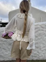 Blusa color crema de algodón con escote en V, tirantes ajustables en la espalda, mangas 3/4 con elástico en los puños y terminación en tul bordado de algodón.