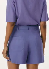 Short de vestir color lila, de corte recto, con bolsillos laterales y cierre frontal con botón y cremallera.
