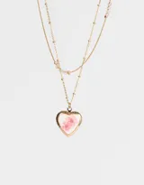 Collar corto dorado de doble cadena, con dije de relicario en forma de corazón con flores rosadas.