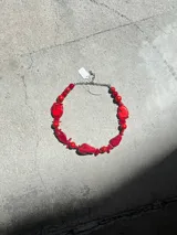 Collar corto con cadena plateada y cuentas de coral rojo de diferentes formas y tamaños.