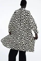 Vestido camisero midi de viscosa con estampado geométrico en blanco y negro. Tiene cuello camisero, tapeta de botones oculta, mangas largas raglán con puños sencillos y costuras fruncidas en la falda. Sin forrar.