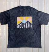 Remera negra con efecto gastado, corte holgado y estampa en la espalda con montañas y la palabra "Mountain" en blanco.