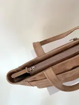 Cartera tipo tote de cuero graneado color negro, con textura uniforme y suave al tacto. Tiene manijas de 55 cm, bolsillo frontal con broche imantado, bolsillo trasero con cierre metálico, cierre principal metálico, forro interior y tres bolsillos internos (uno con cierre, uno plaqué y uno tipo sobre con solapa y botón).