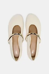 Zapato tipo bailarina color crema con tira sobre el empeine y aplique metálico dorado.