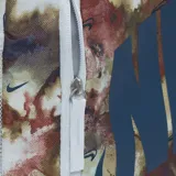 Mochila Nike Elemental con estampado abstracto en tonos beige, marrón y rojo. Logo de Nike en azul. Incluye un compartimento principal con cierre, un bolsillo frontal con cierre, un bolsillo lateral de malla y un estuche desmontable para lápices.
