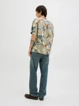 Camisa de manga corta con estampado de hojas en tonos beige, azul y marrón. Tiene cuello resort, cierre con botones y corte relajado.