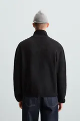 Cárdigan negro de punto con cuello alto, cierre frontal con cremallera, bolsillos laterales y mangas largas.