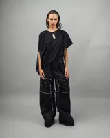 Pantalón negro de corte holgado con múltiples correas y ojalillos metálicos.