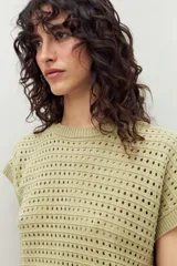 Chaleco tejido color crudo con diseño calado, cuello redondo y mangas cortas. Corte holgado.