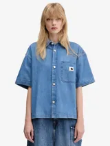 Camisa de denim azul claro de Carhartt WIP, corte relajado, manga corta, cuello camisero, cierre frontal con botones y bolsillo de parche en el pecho con logo de la marca.