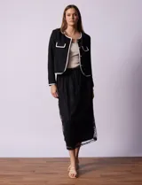 Chaqueta de tweed blanca con ribete negro, escote a la base, abertura central con botones, bolsillos delanteros y puños con aplique de botones perlados.