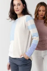 Buzo de tejido fino, manga larga, con diseño de bloques de color y rayas horizontales en tonos beige claro, celeste y lila. Presenta cuello redondo.