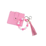 Llavero con pulsera de cuentas rosas y blancas, tarjetero rosa con cierre a presión y borla de flecos rosa.