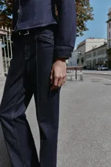 Jeans de mezclilla azul oscuro, tiro medio, corte recto y slim. Presenta costuras verticales marcadas en el frente de ambas piernas y viene con un cinturón de cuero marrón.