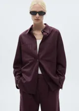 Camisa color borgoña con finas rayas verticales, de corte oversize, manga larga con puños abotonados, cuello camisero y dos bolsillos de parche en el pecho.