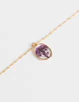 Cadena corta dorada con dije circular transparente que contiene una flor amarilla.
