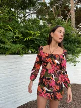Vestido corto con estampado floral en tonos marrones, naranjas, rosas y verdes. Tiene escote cuadrado con detalle fruncido en el centro, mangas largas abullonadas y falda con tajo lateral.