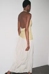 Vestido largo de fiesta con cuello halter fluido y hombros descubiertos. Presenta un top dorado drapeado y una falda larga color crema con textura.