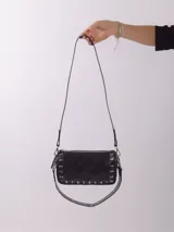 Bandolera color rojo de cuero con tachas plateadas. Tiene dos asas desmontables, una corta con tachas para llevarla en la mano o al hombro y una larga para llevarla al hombro o cruzada. Tiene bolsillo interior con cierre y forro.