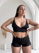 Short negro ajustado con cintura ancha adornada con tachas plateadas y lazos laterales.