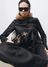 Chaqueta negra de cuero ovino con cuello de solapa, diseño recto, dos bolsillos de parche con solapa en la parte delantera y cierre delantero con botones.