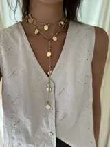 Collar largo de cordón color beige con cuentas doradas y dijes de monedas doradas.