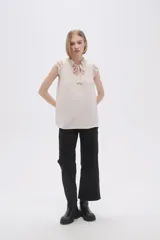 Blusa sin mangas color crudo con cuello con lazo y volados en los hombros.