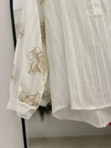 Blusa blanca con escote en pico y botones en el frente. Detalles florales bordados en mangas.