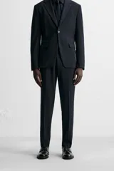 Pantalón de vestir azul marino, de corte slim fit, con bolsillos laterales y traseros. Se ajusta a la cintura con cinturón de cuero marrón.